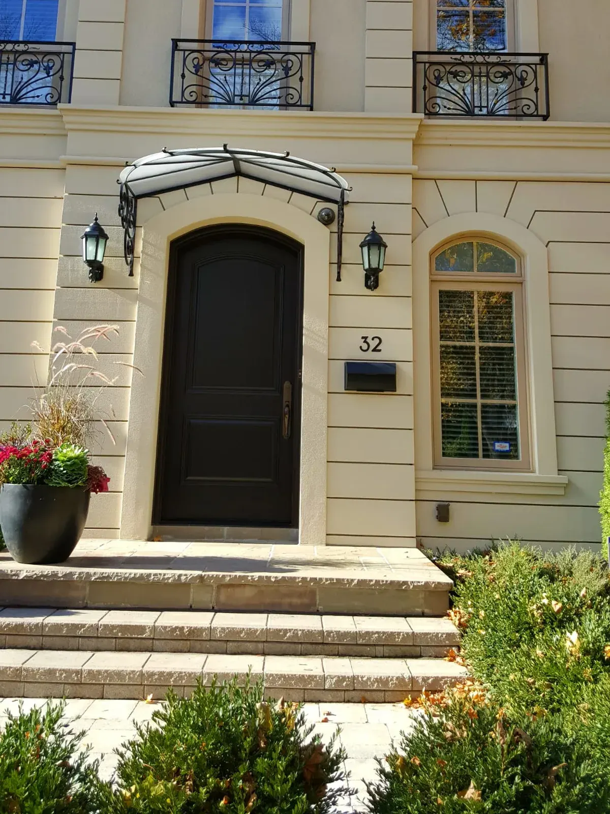 Arched front entry with a black panel door, stucco surround and stone steps