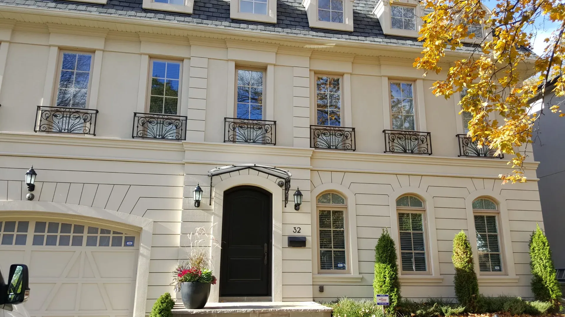 Full front elevation of a cream stucco residence with layered banding, arched windows and iron balconies