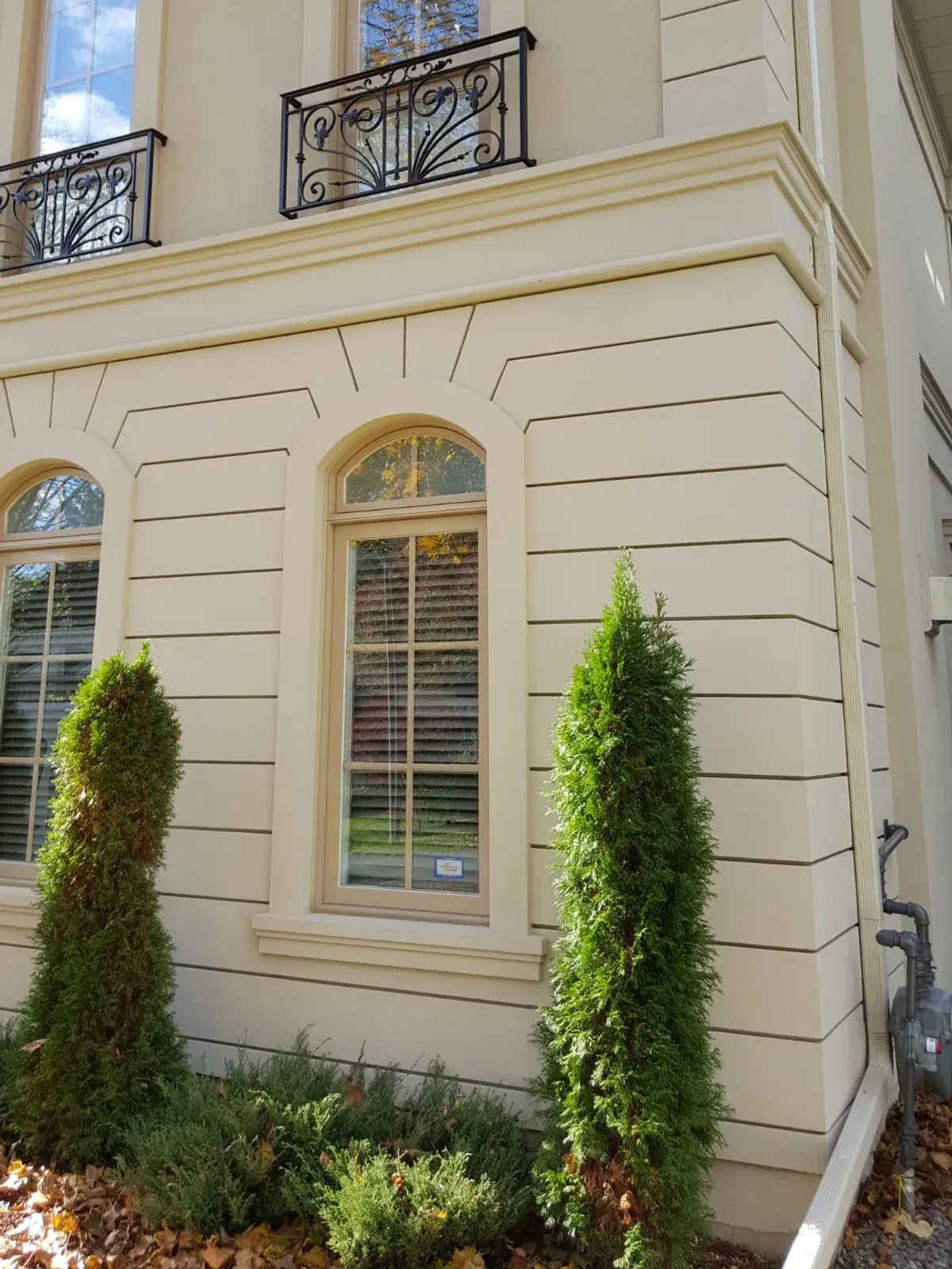 Arched window with stucco surround, level banding and a wrought-iron balcony above