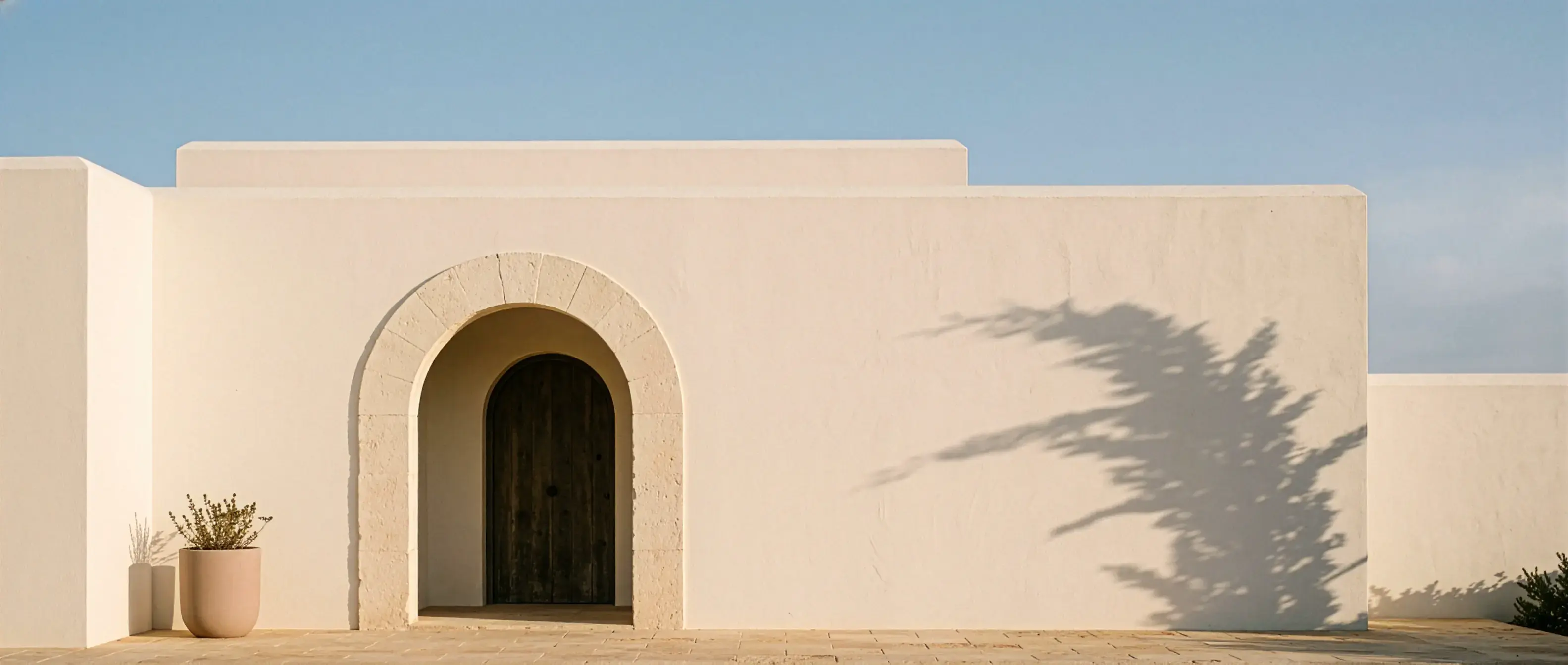Minimalist white stucco house with a stone arch entrance under a clear sky