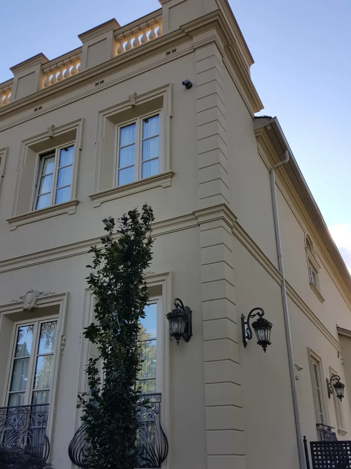 Corner of a cream stucco residence with layered horizontal banding and a carriage lantern